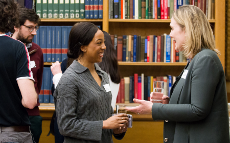 UCD alumni and current students networking at an event, library bookshelves in the background.
